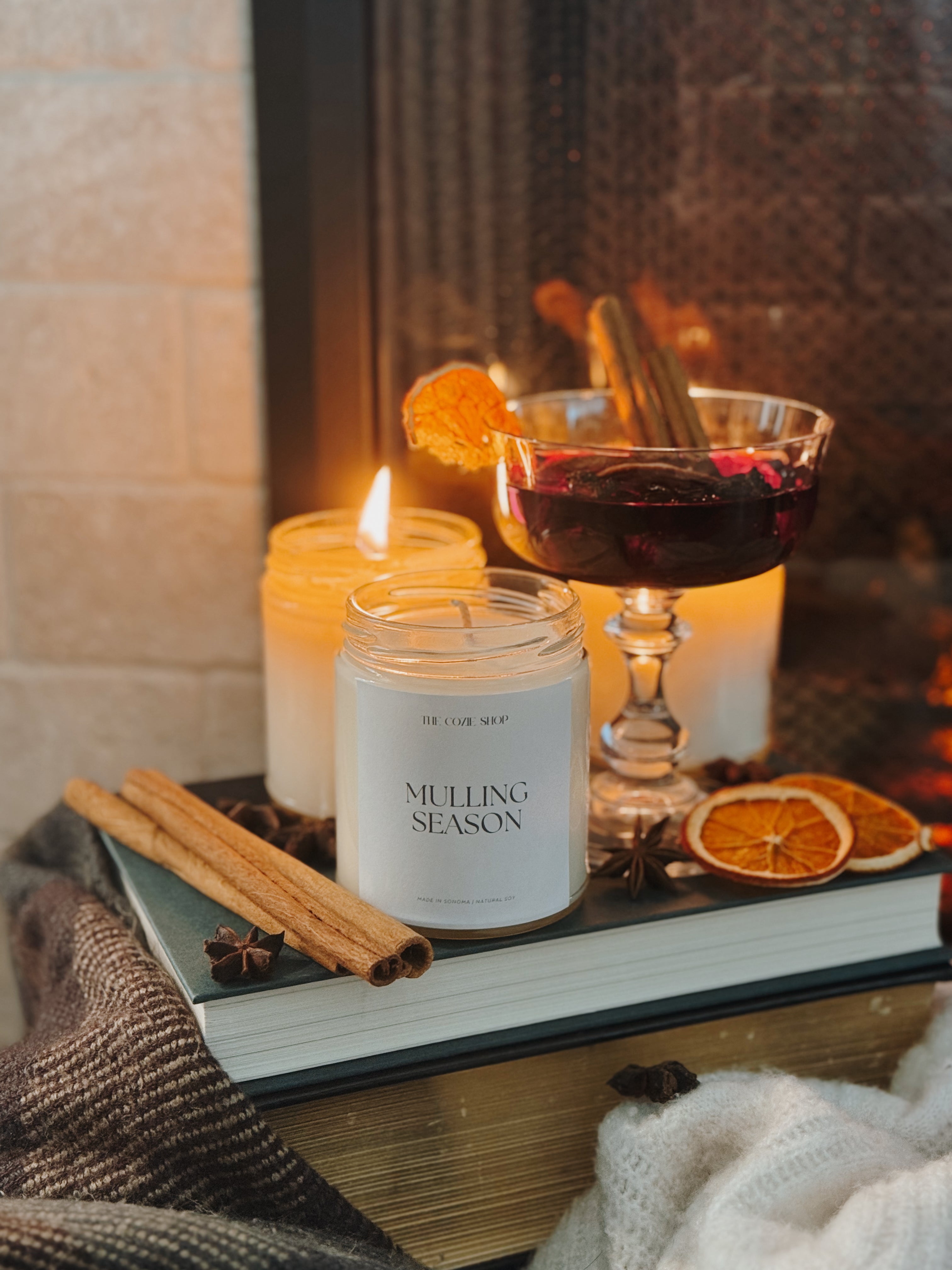 Candle labeled 'Mulling Season' on a book with mulled wine and spices in the background.