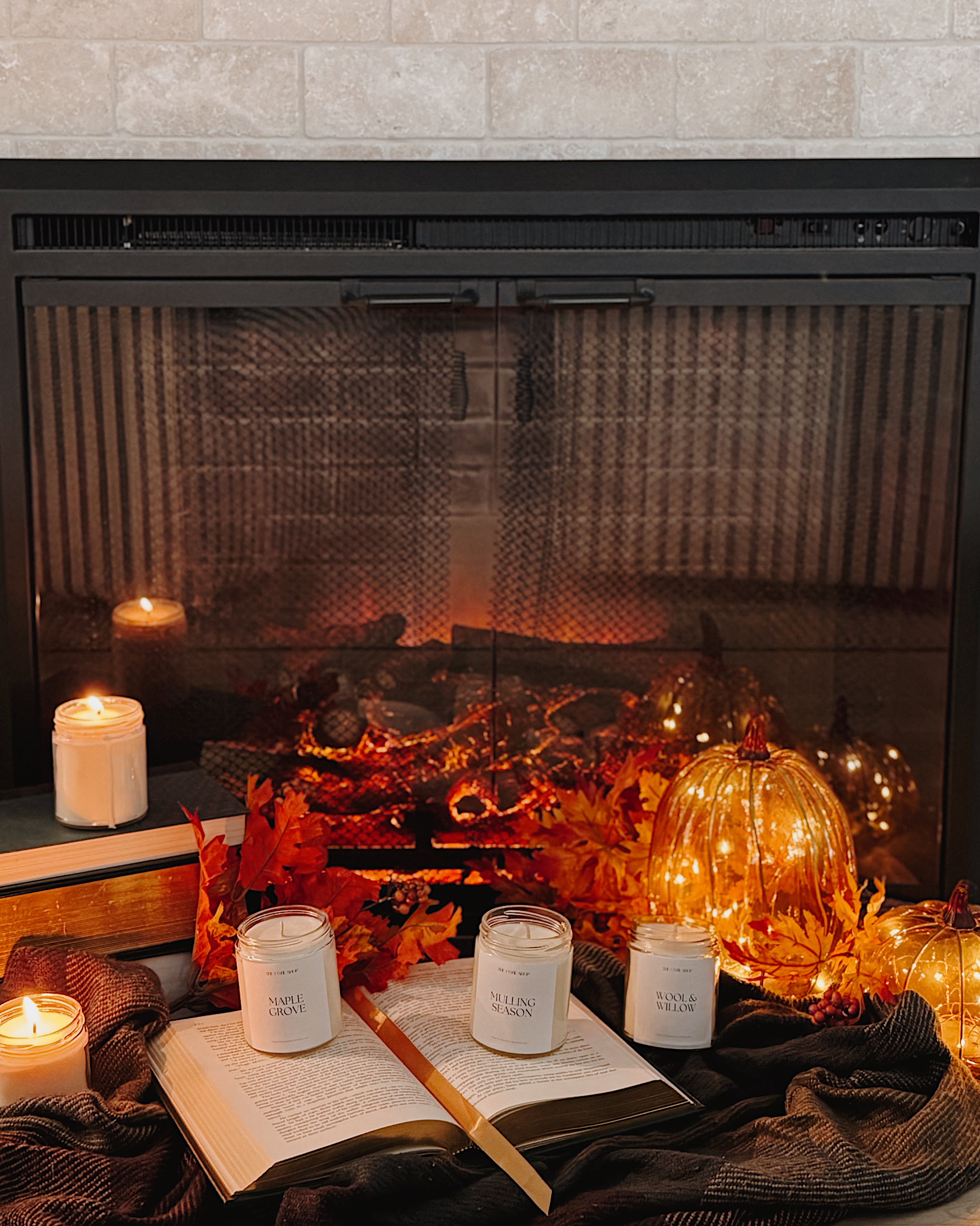 Cozy fireplace scene with candles, books, and decorative pumpkins.