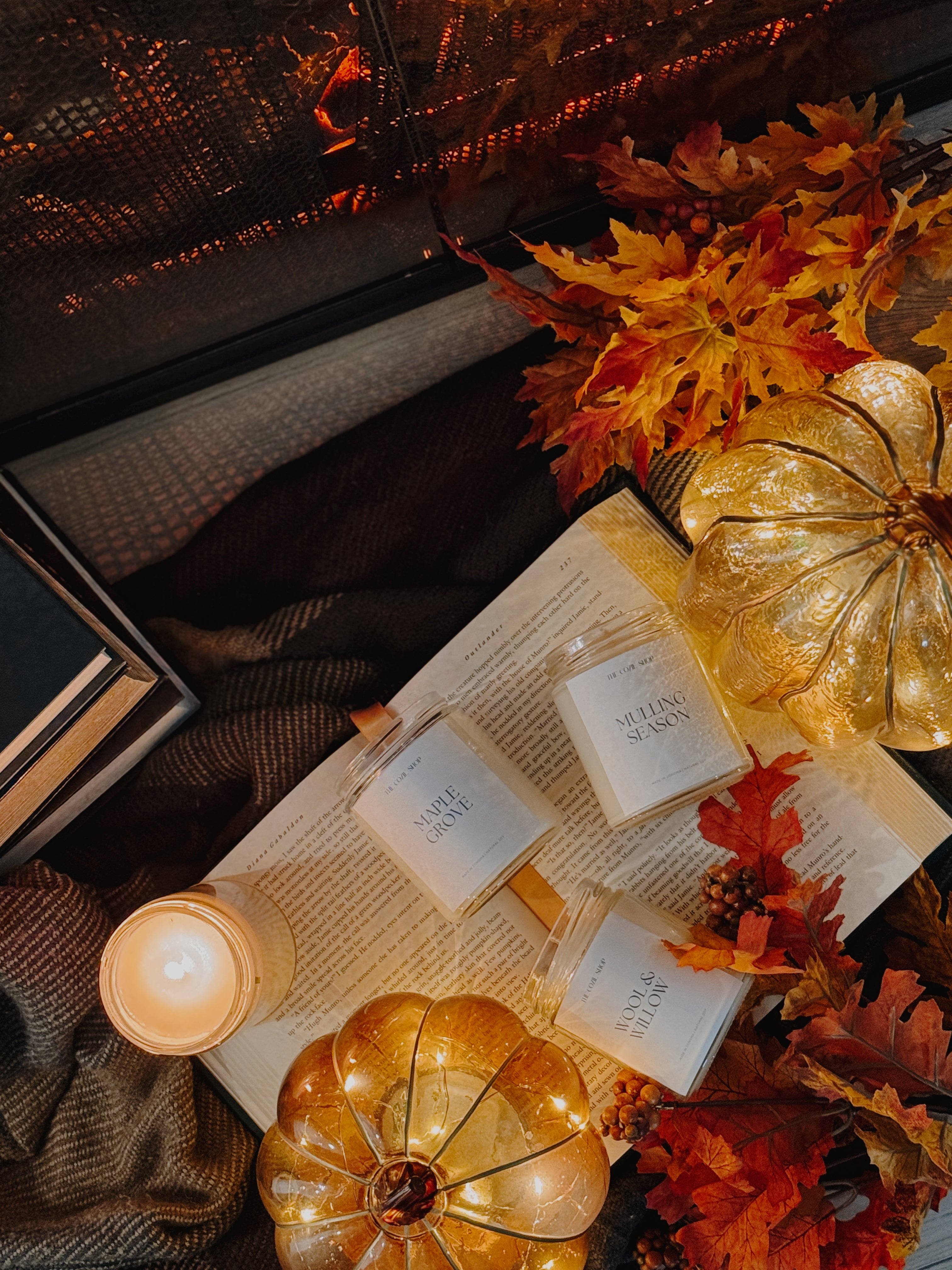 Autumn-themed setting with candles, pumpkins, and books by a fireplace.