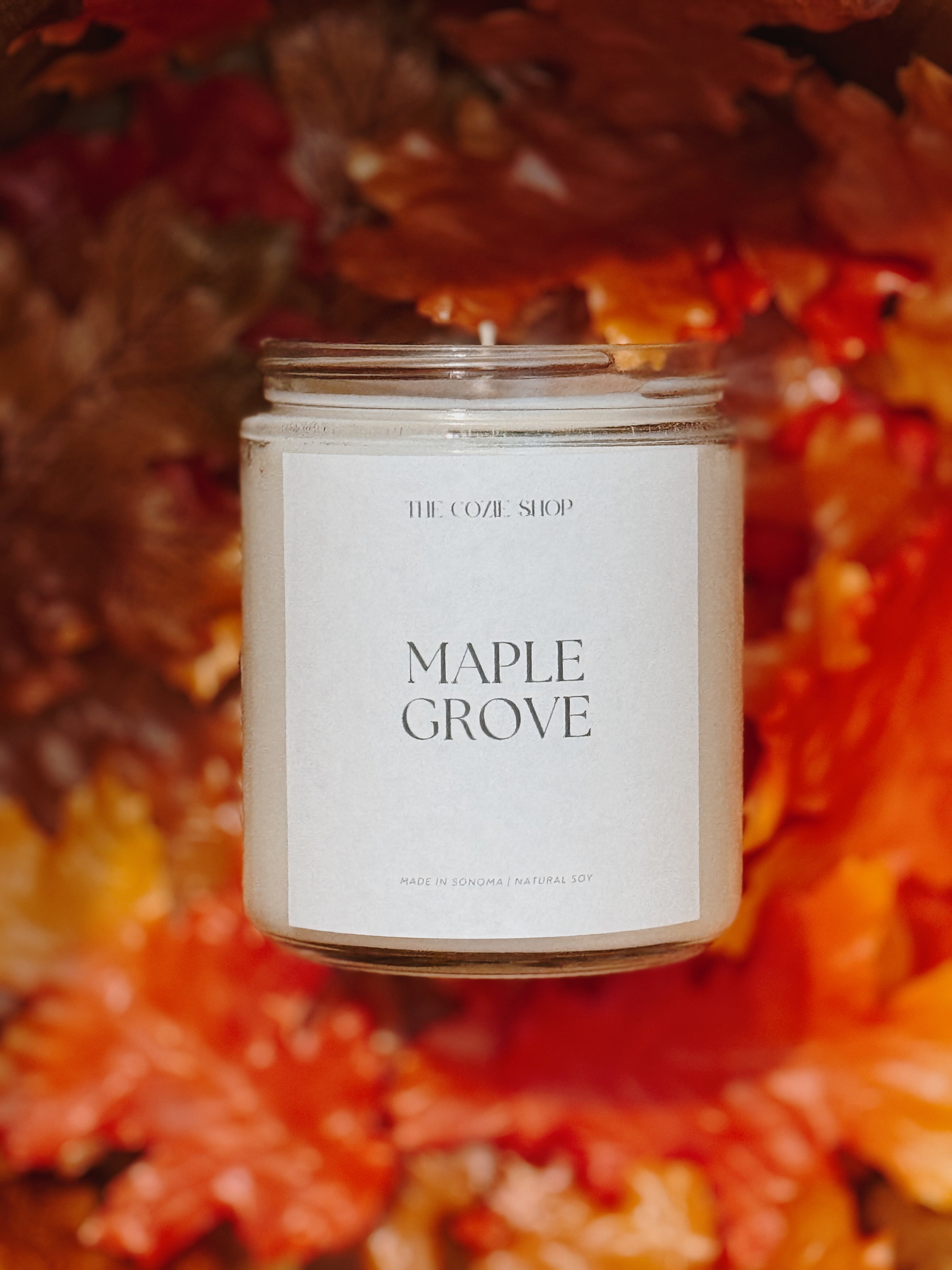 Candle labeled 'Maple Grove' surrounded by autumn leaves