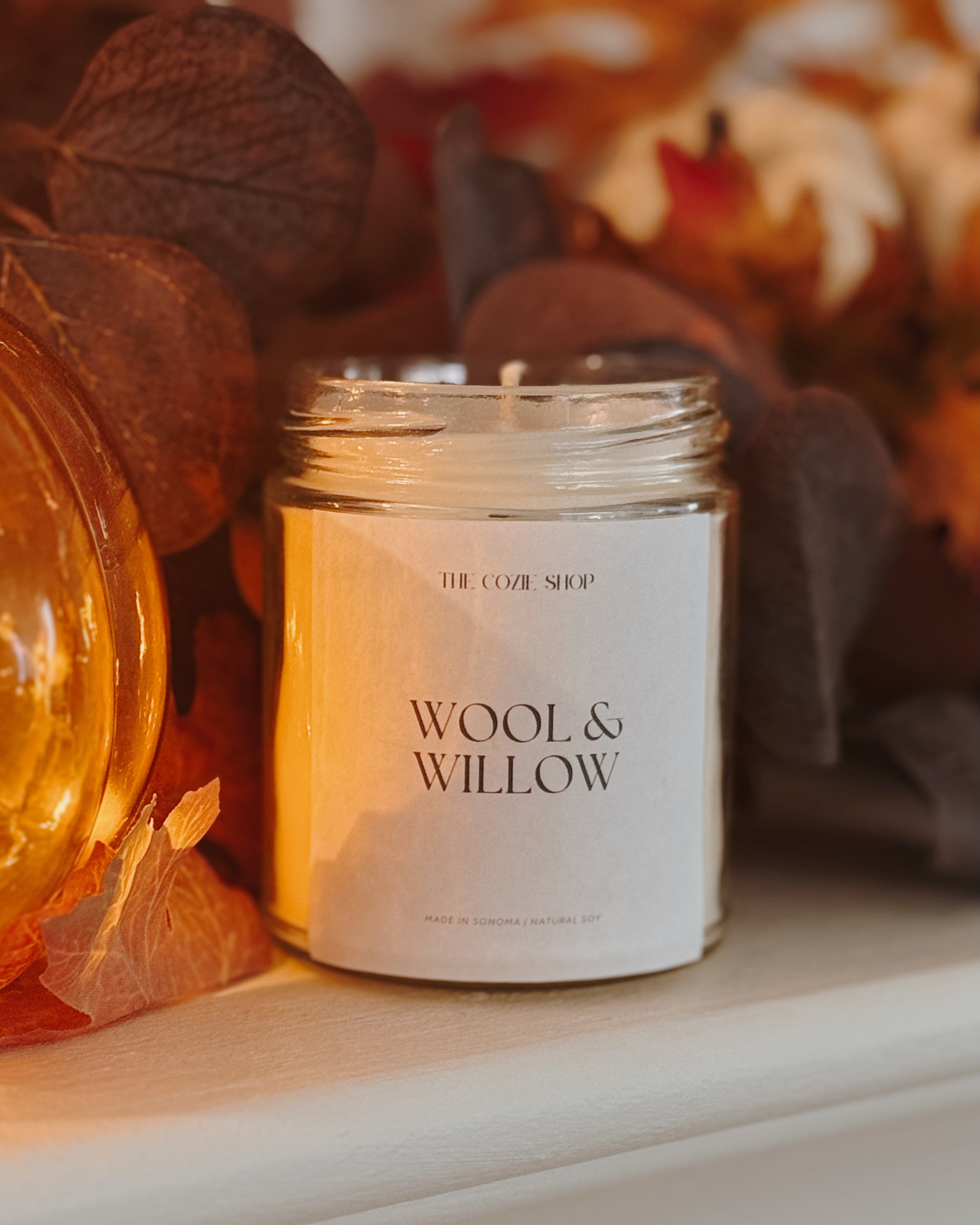 Candle labeled 'Wool & Willow' with autumn leaves in the background